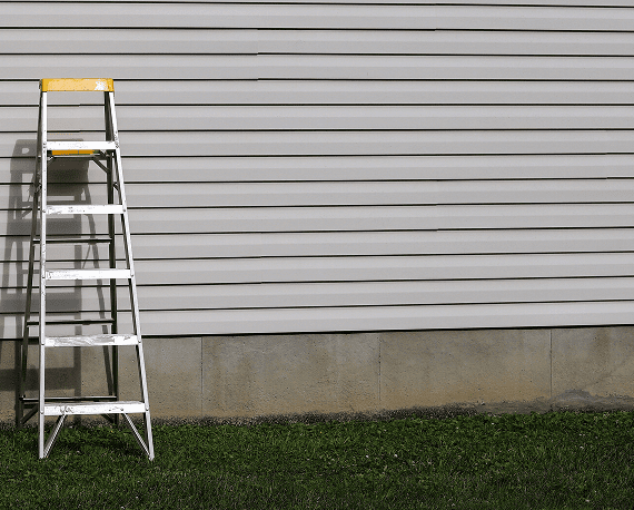 A ladder leaning against a house with white siding and a grassy yard.
